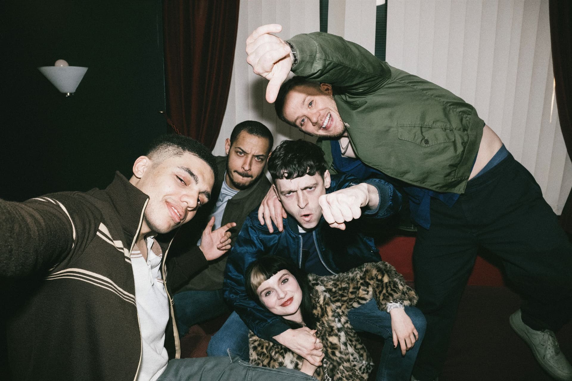 Group of friends posing energetically in a room with curtains