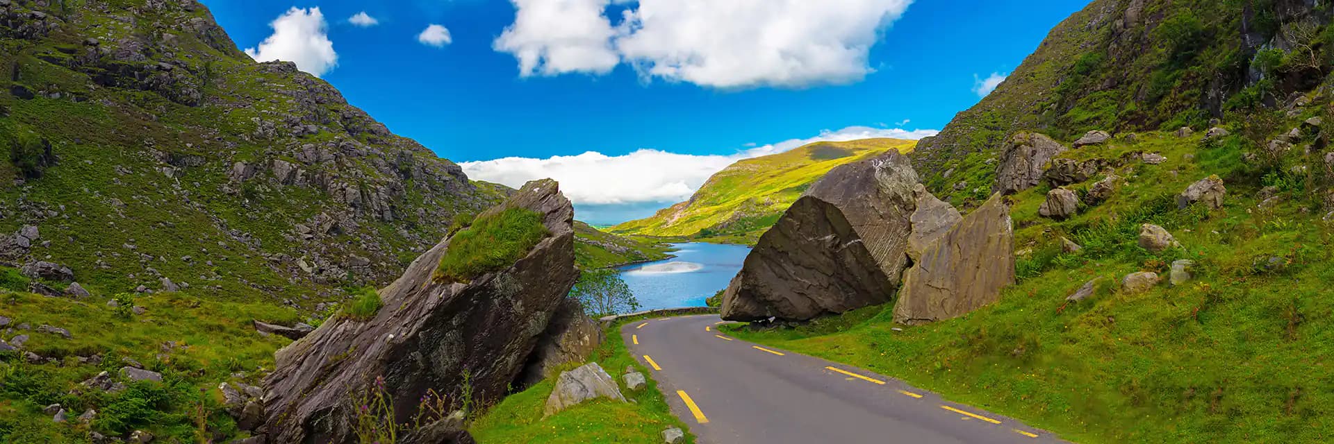 Winding road through lush green valley with lake and cliffs