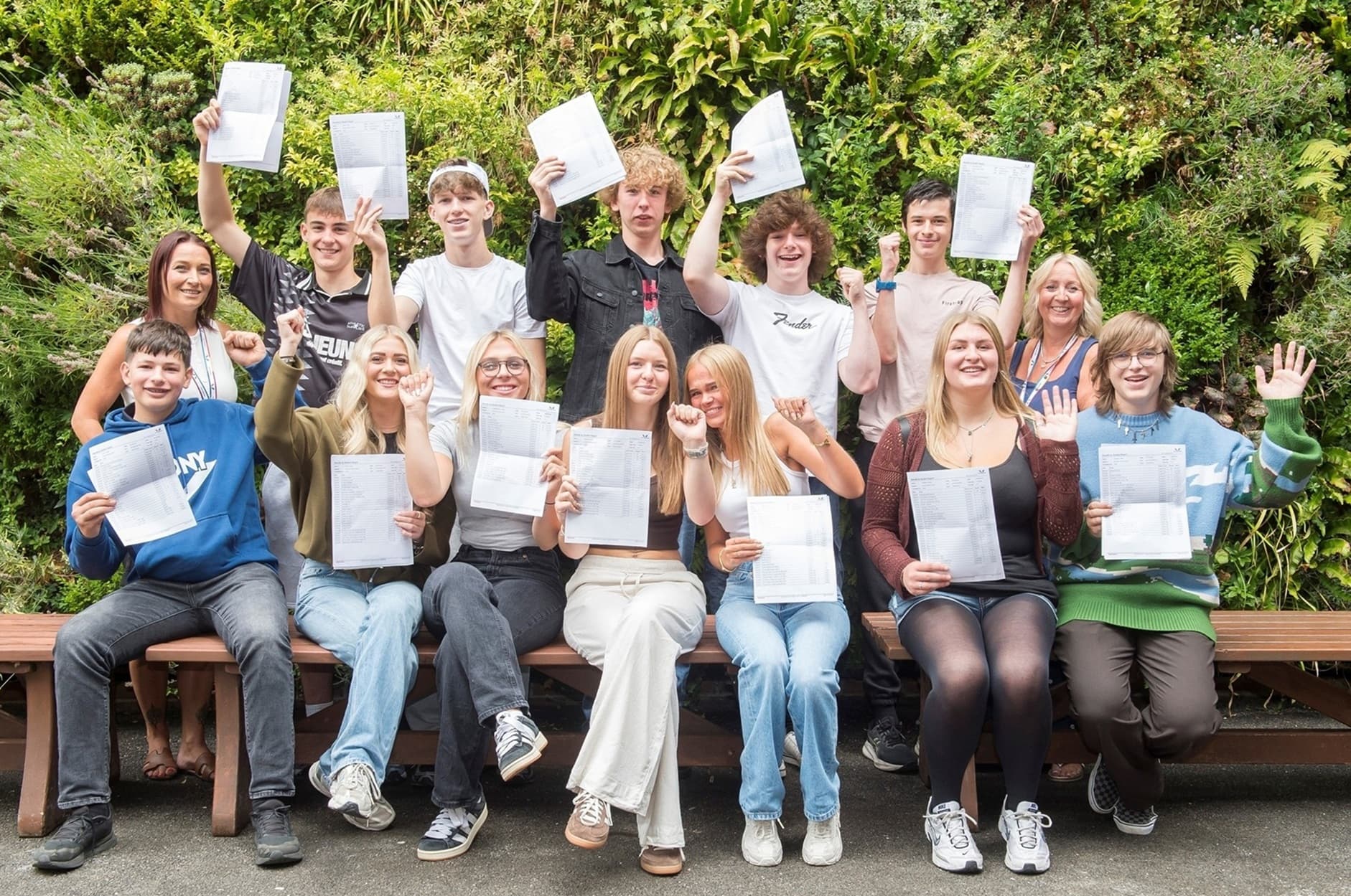 Group of students celebrating exam results with certificates outdoors