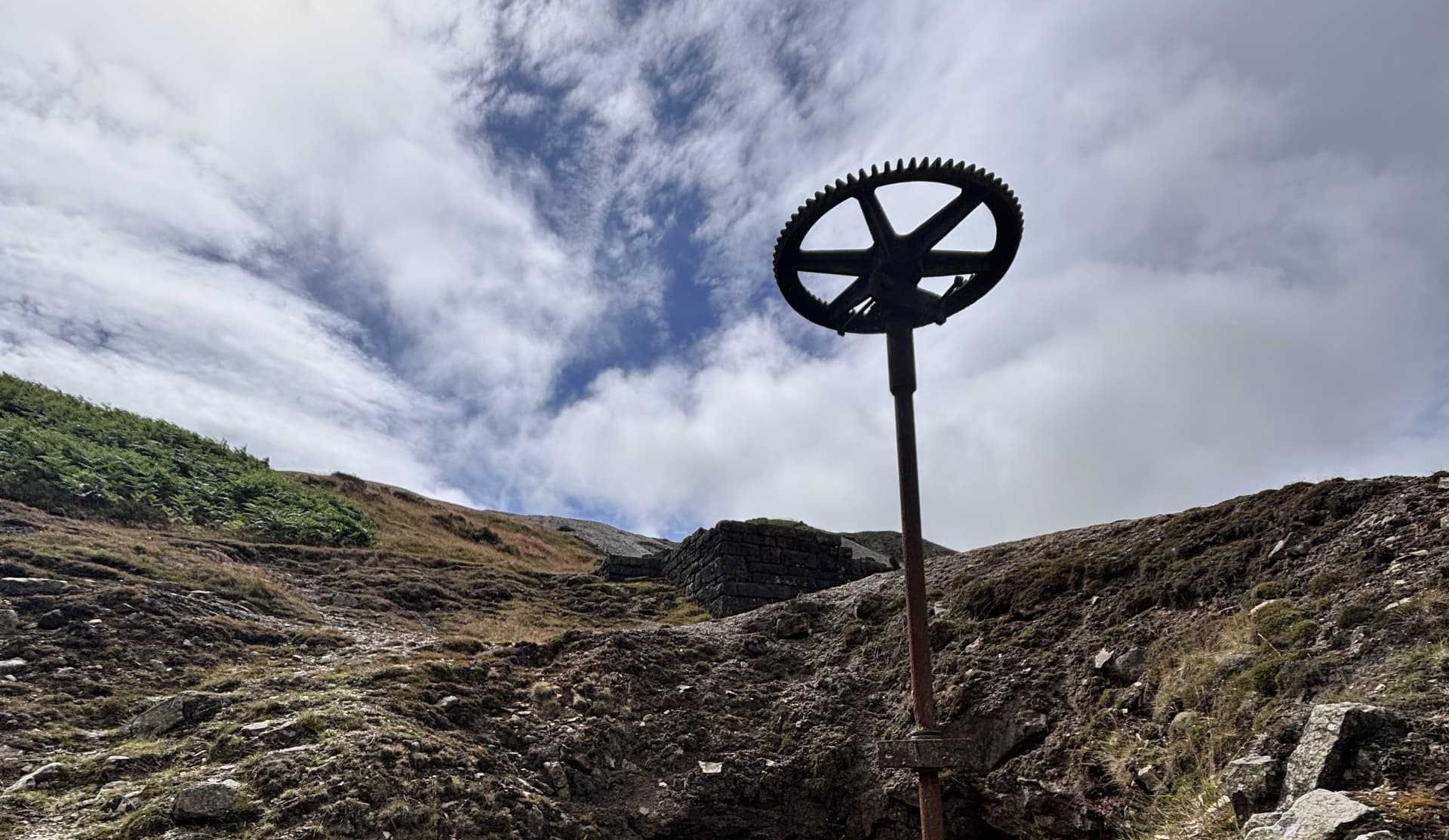 Old mining wheel on rocky landscape under cloudy sky