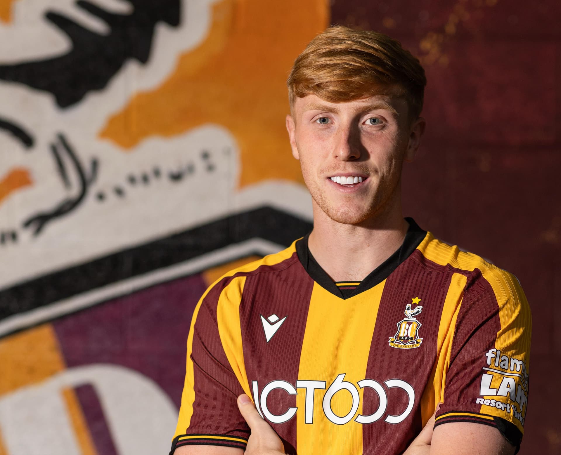 Smiling footballer in claret and amber kit against mural