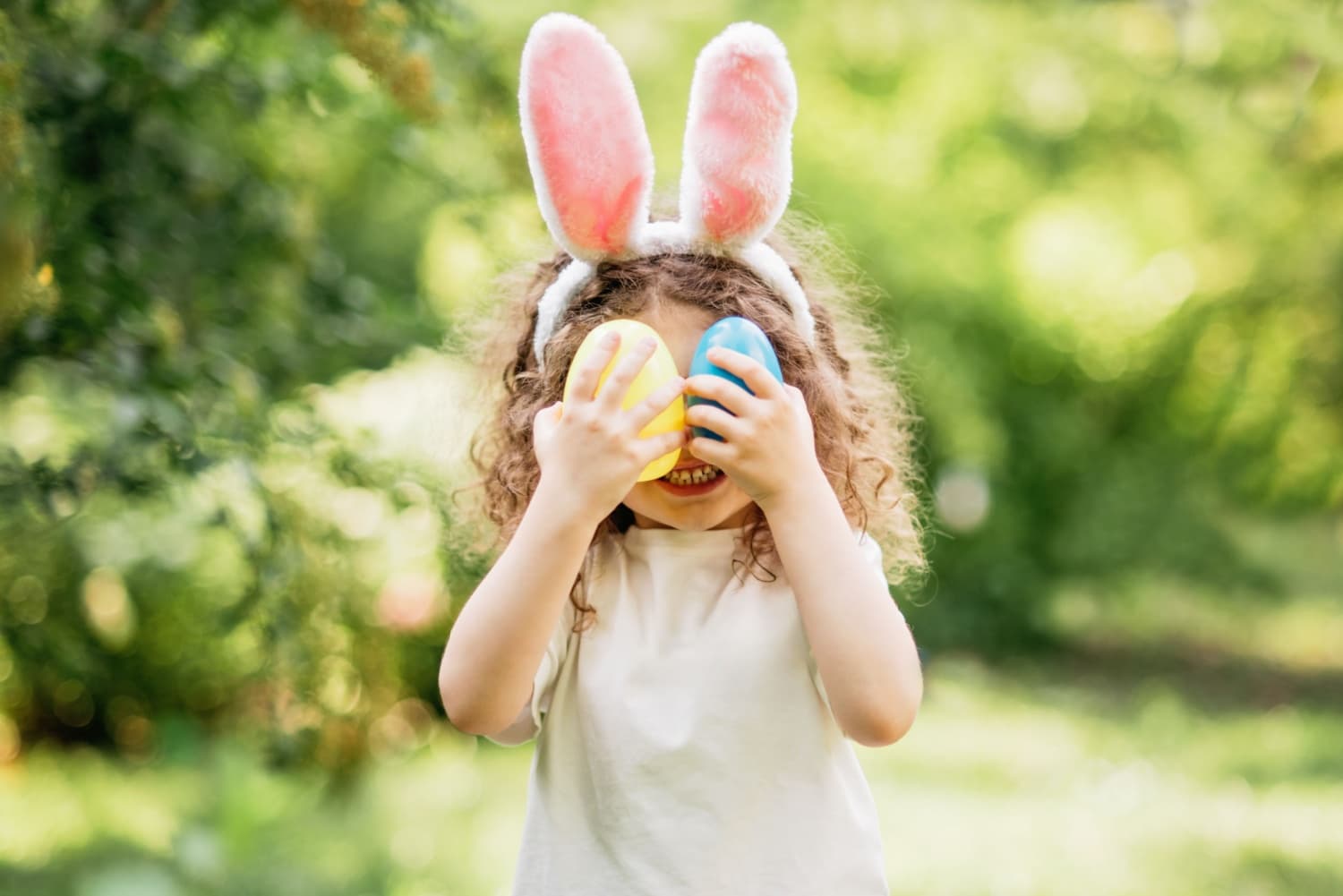Child with bunny ears holding colorful eggs in garden