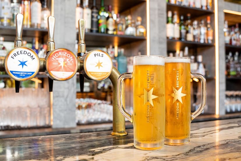 Two frosty pints of lager with star logos sit on a polished bar top, surrounded by shelves of spirits in a vibrant Sheffield pub.