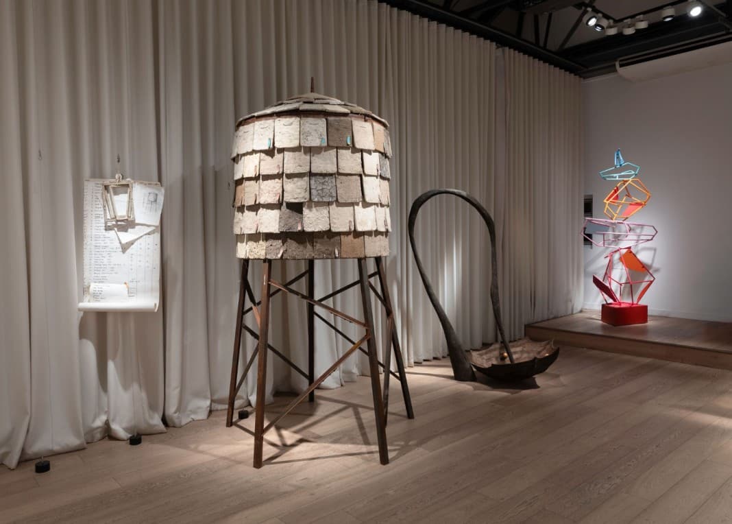 Contemporary art installation featuring a wooden structure, metal sculptures, and a minimalist display in a gallery setting.