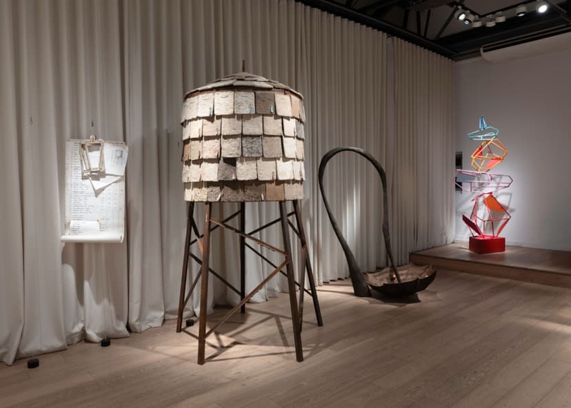 Contemporary art installation featuring a wooden structure, metal sculptures, and a minimalist display in a gallery setting.