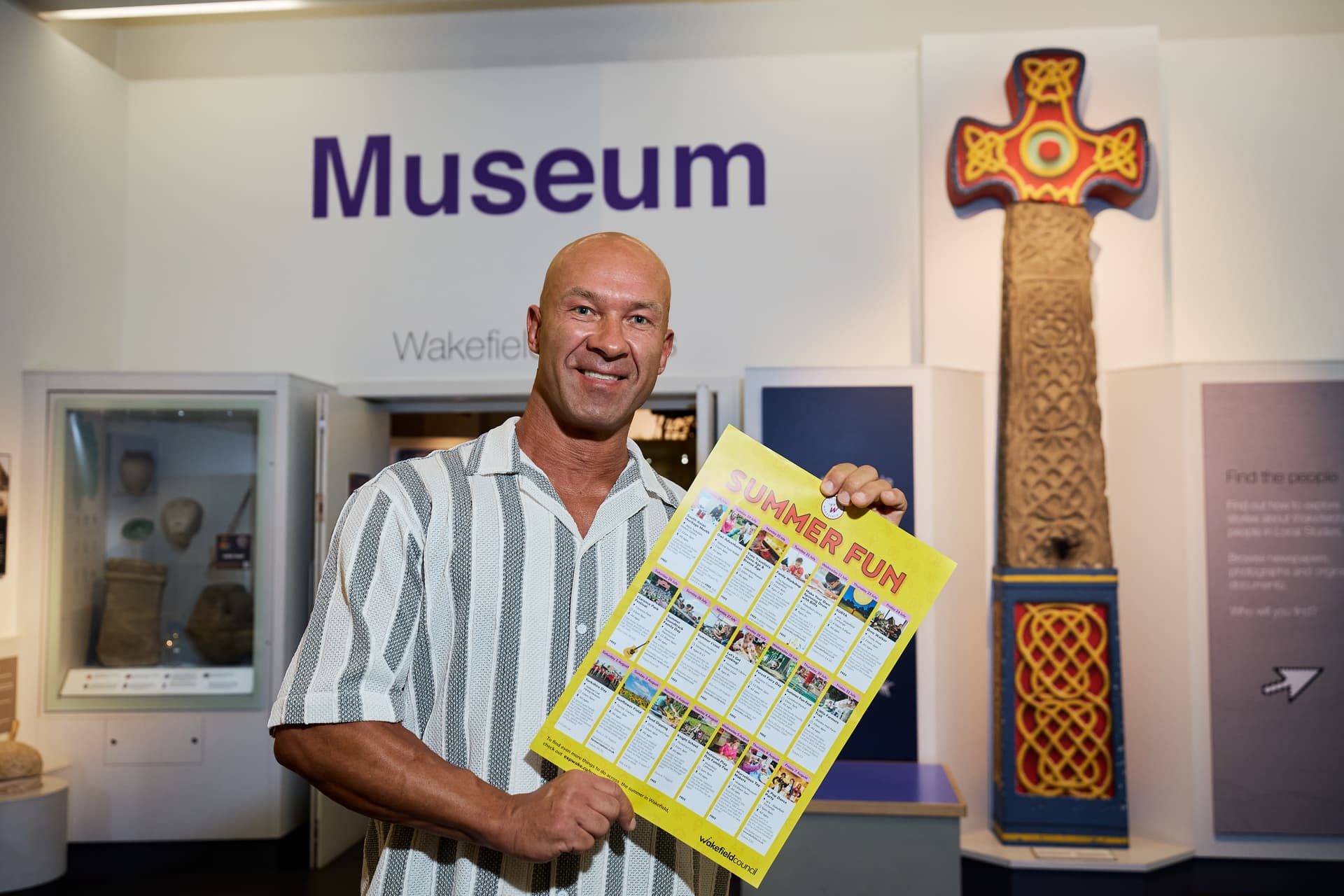 Smiling man holds summer events poster in Wakefield Museum