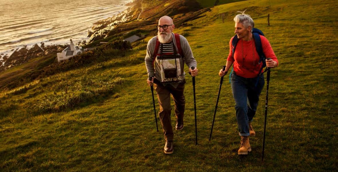 Senior couple hiking on grassy cliffside at sunset