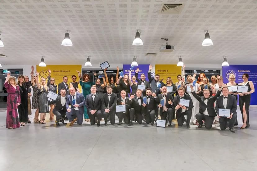 Celebratory group of award winners in formal attire, holding certificates, in a modern venue with colorful banners.