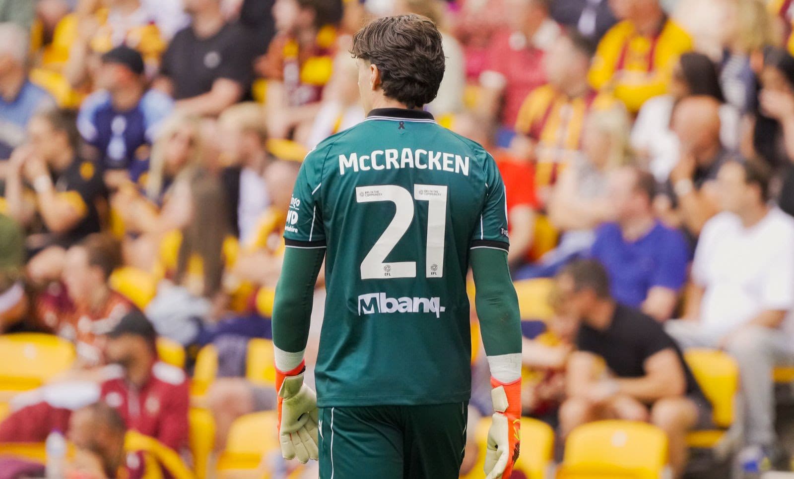 Football player in green kit with number 21 at crowded stadium