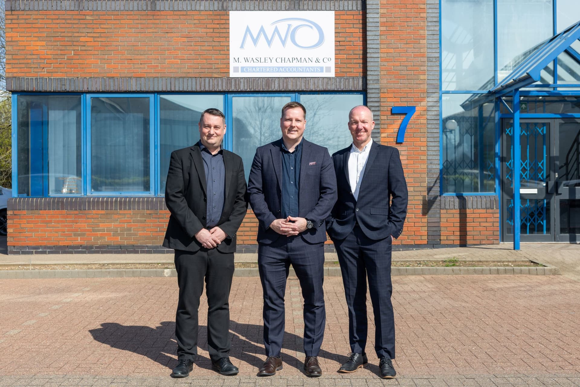 Three men in suits standing outside a modern brick office building