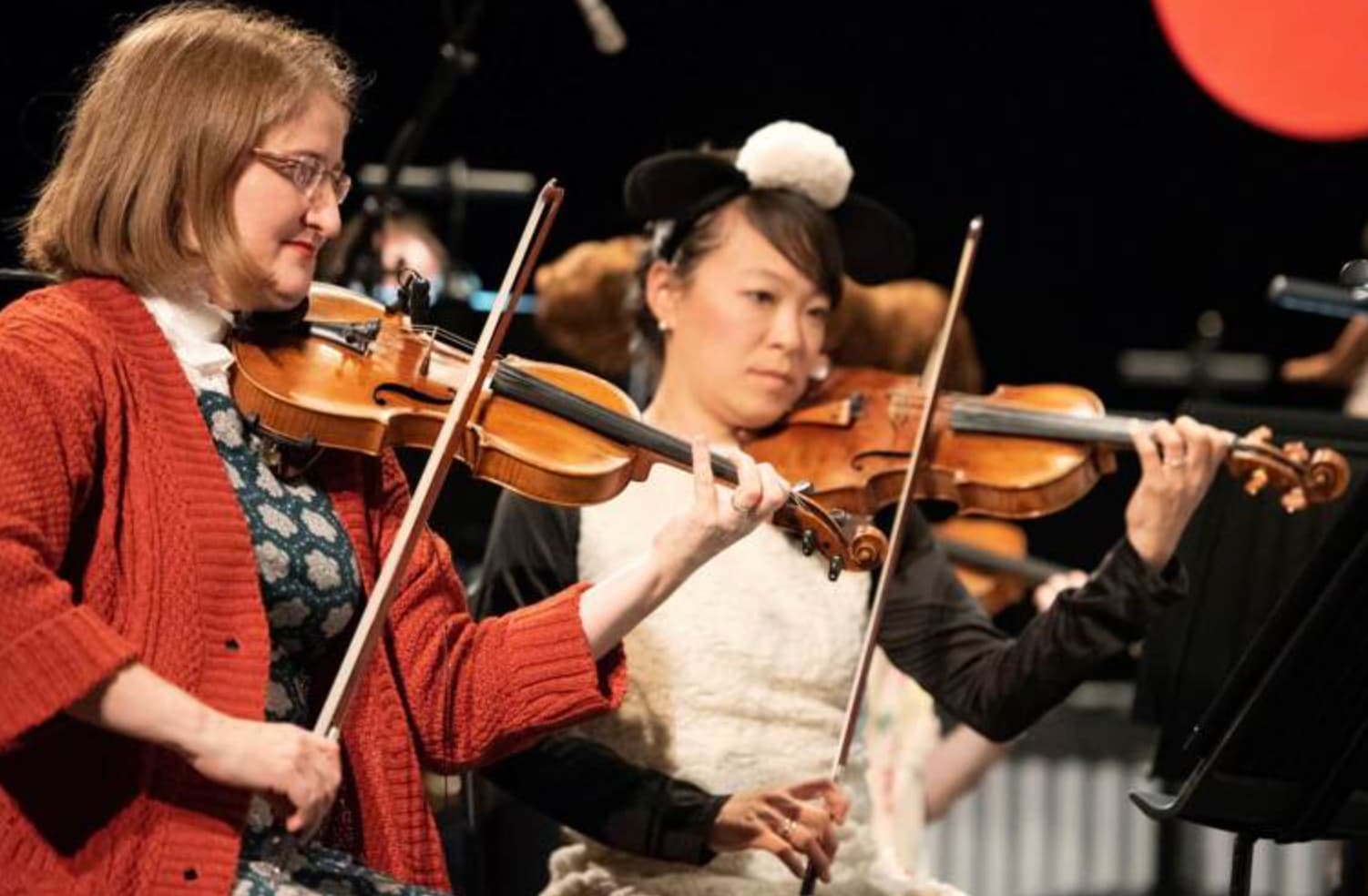 Two violinists, one in red sweater, one in costume, performing
