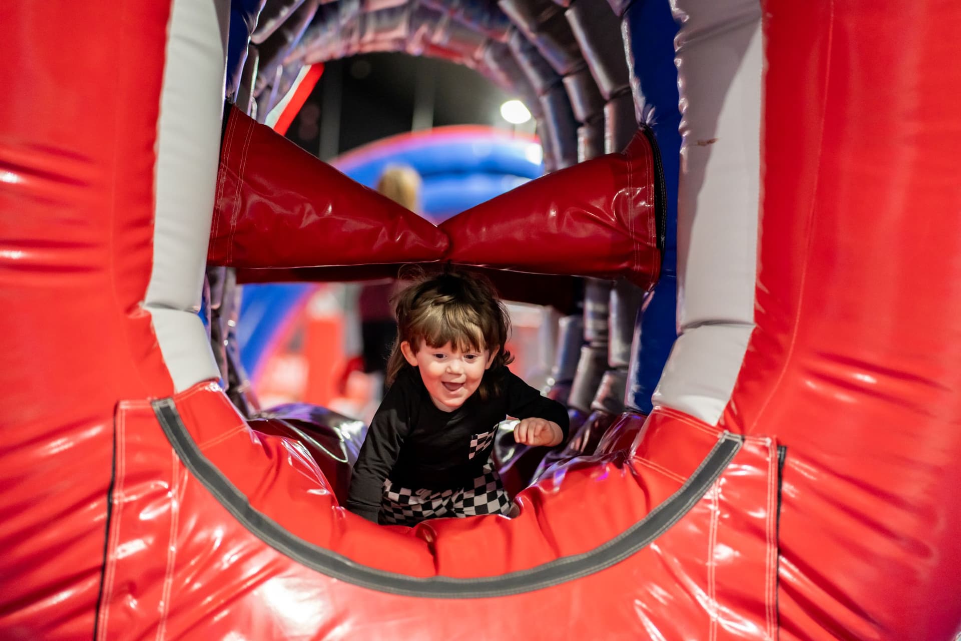 Child crawling through inflatable red tunnel at play center