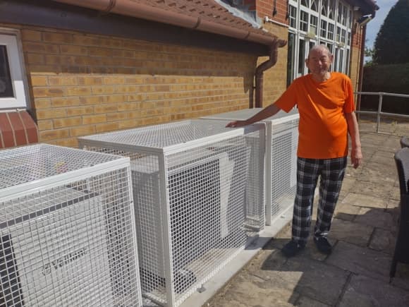 Elderly man in orange shirt standing by air conditioning units