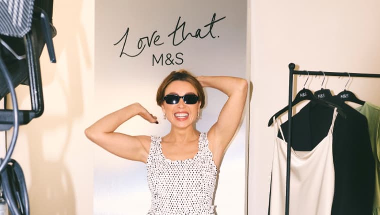 Smiling woman in sunglasses posing beside clothing rack