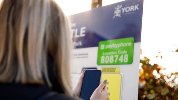 Person using smartphone at York parking sign in autumn