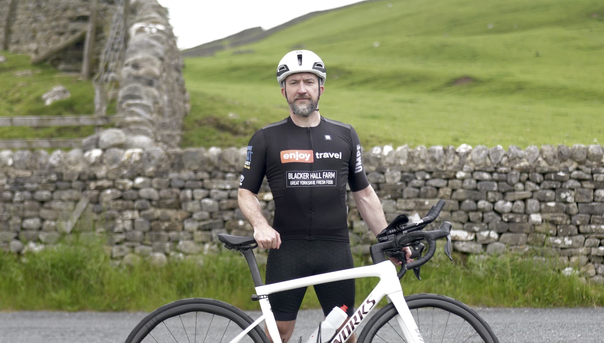 Cyclist in black gear and helmet by stone wall in Yorkshire countryside