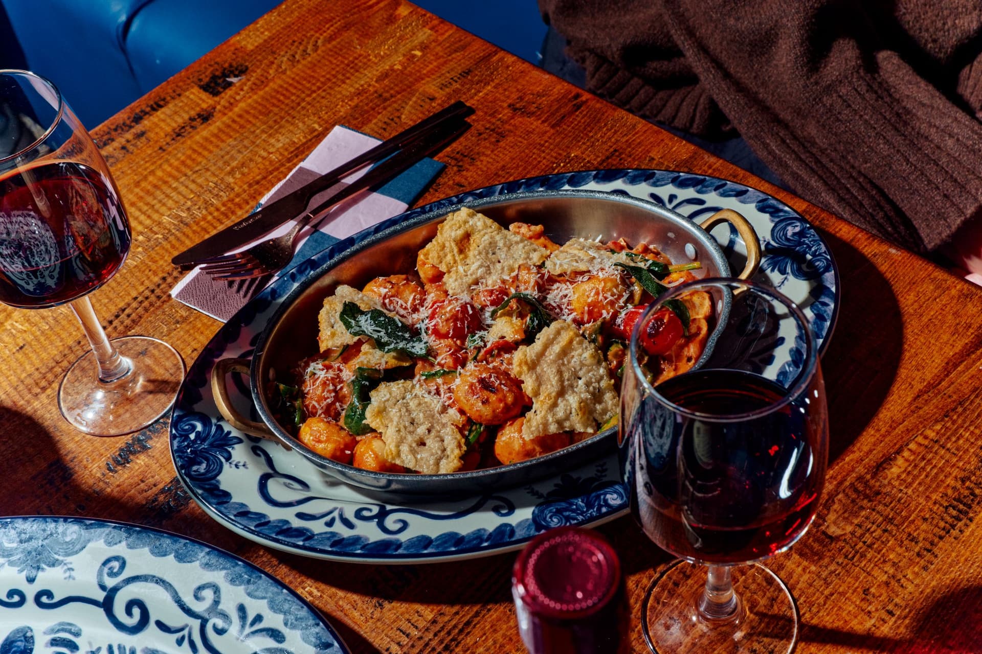 Rustic wooden table with a dish of gnocchi, vegetables and wine