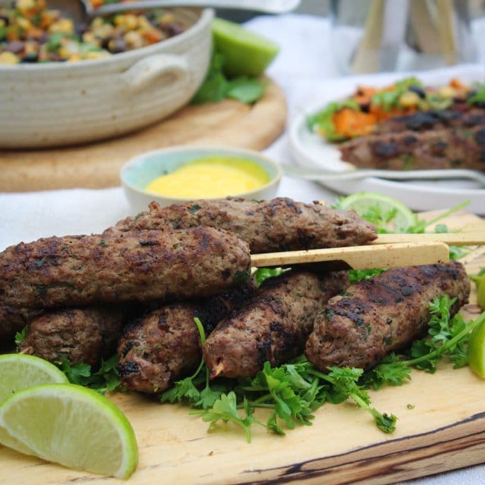 Grilled kebabs on a wooden board, garnished with fresh herbs and lime wedges, set against a vibrant summer picnic backdrop.