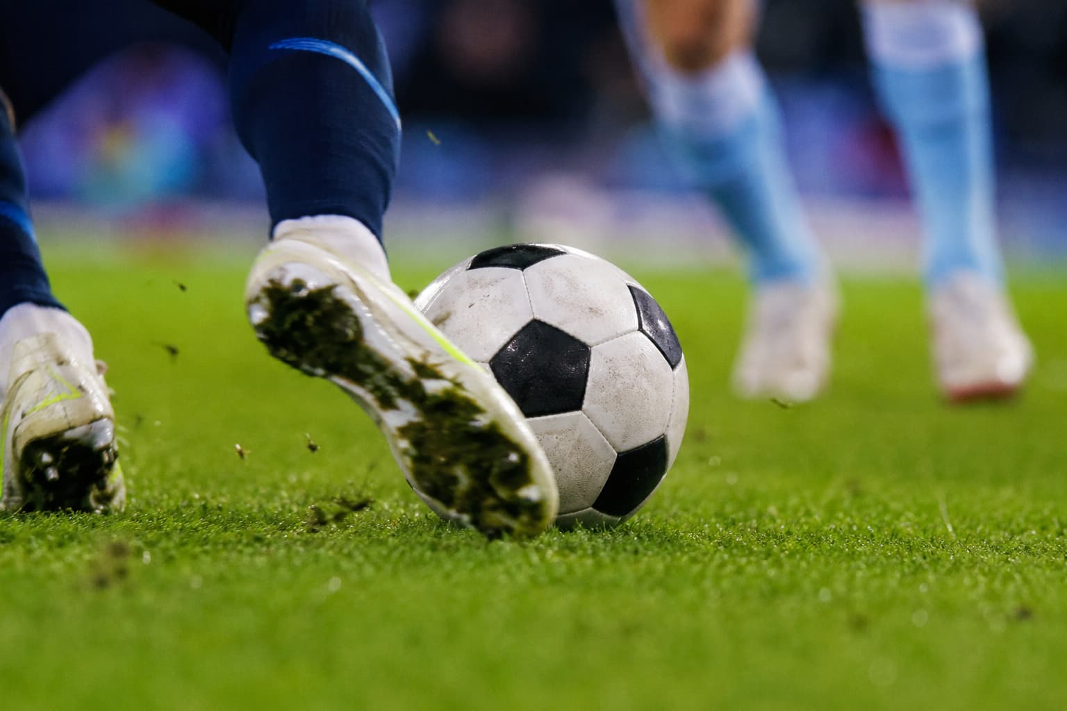 Close-up of footballer's muddy cleats kicking a football on grass
