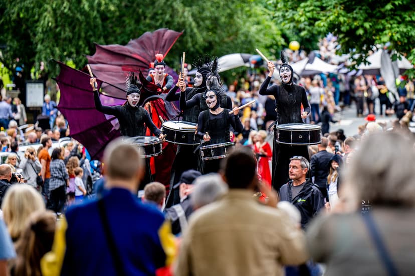 Street performers in black costumes play drums, surrounded by a vibrant crowd in Harrogate, creating a festive atmosphere.