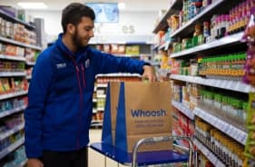 Man in blue jacket placing groceries into a paper bag in a supermarket