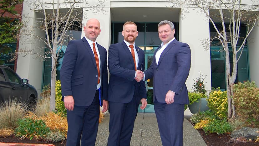 Three men in suits shaking hands outside modern office building