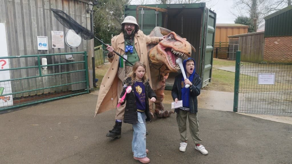 A costumed guide holds a net beside a dinosaur model, with excited children posing at the Tropical Butterfly House in Yorkshire.