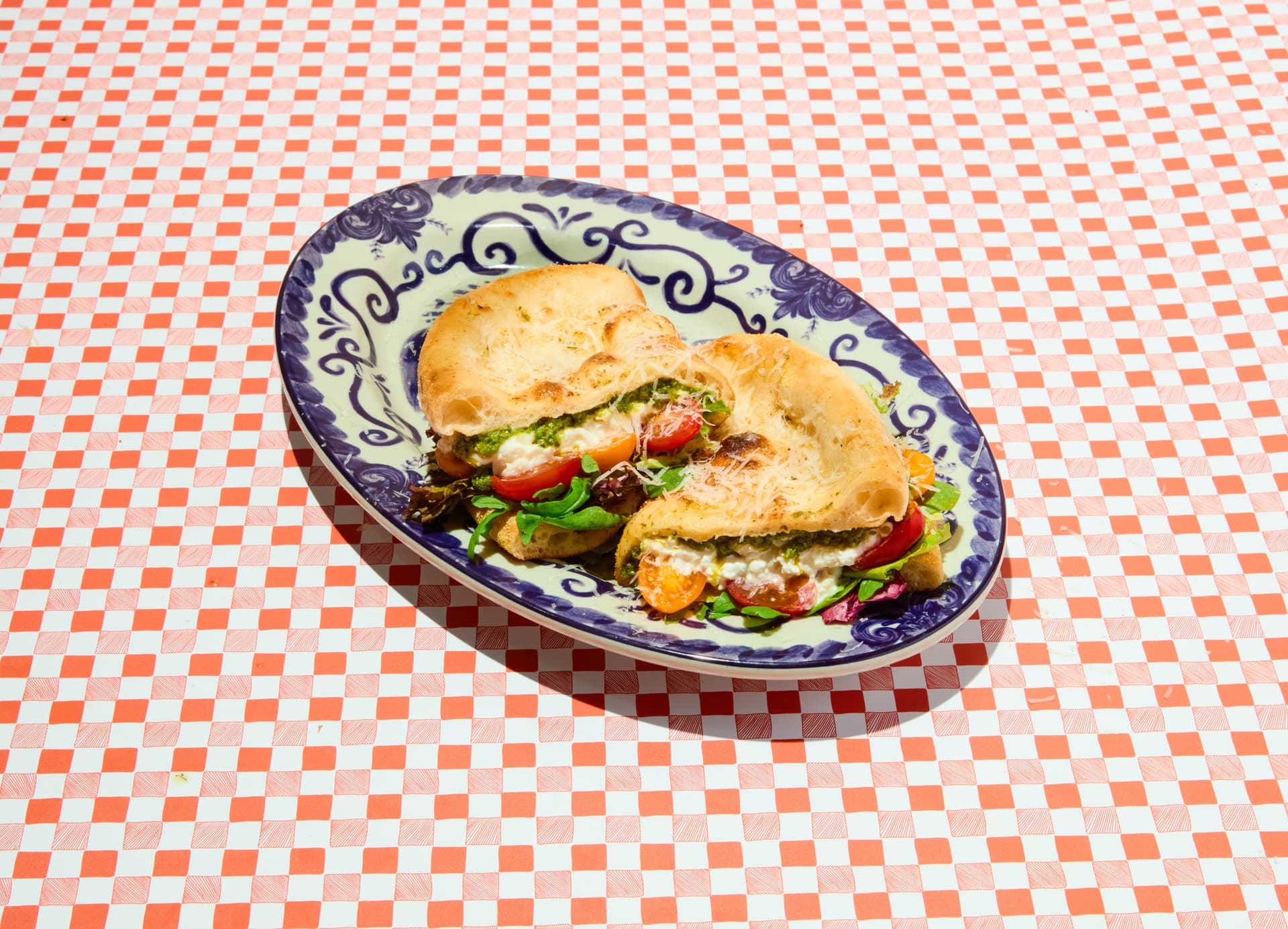 Two sandwiches with greens and tomatoes on a patterned plate