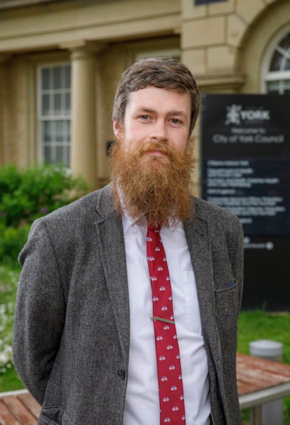Person in suit with red tie standing by York Council sign