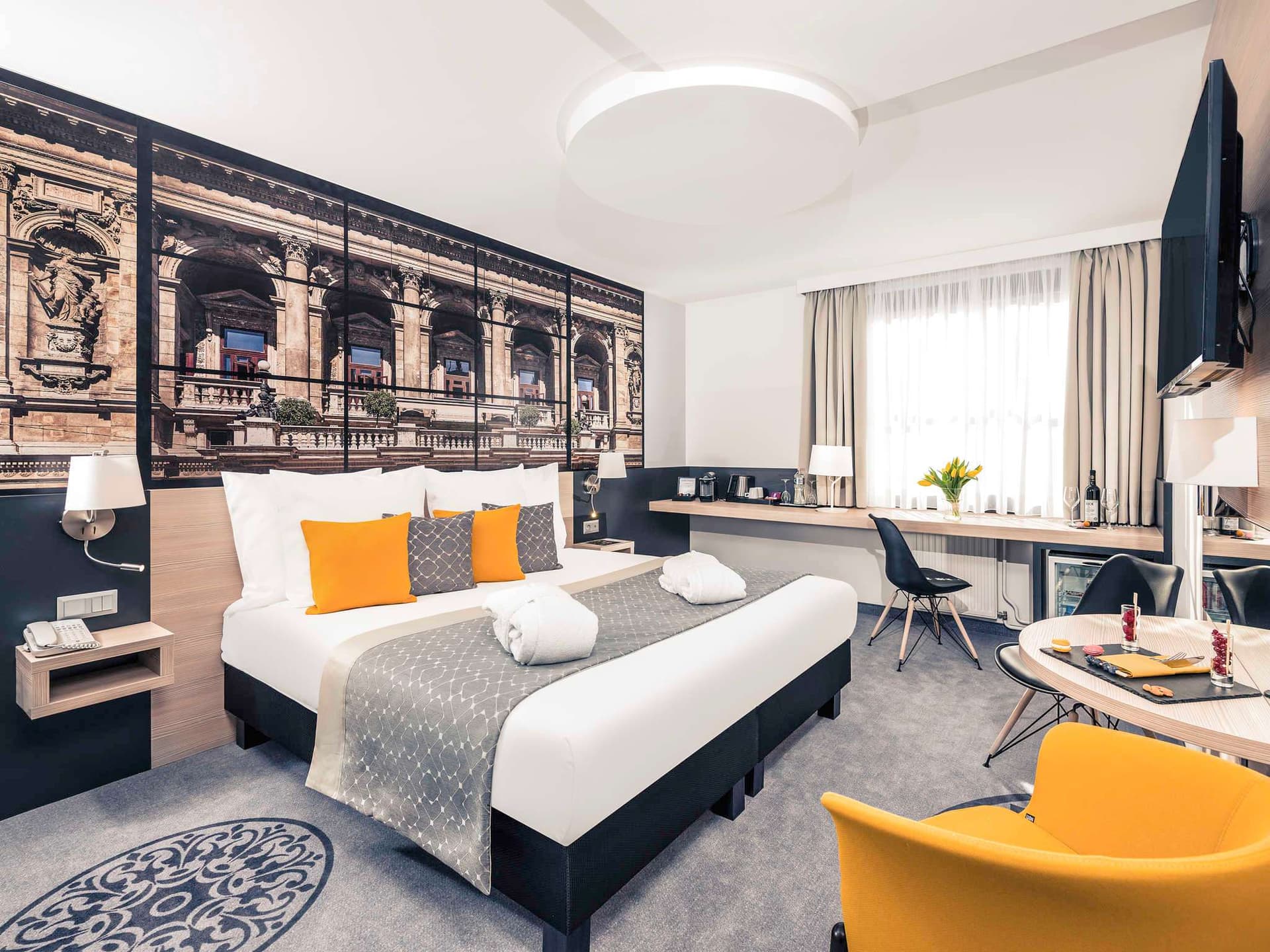 Modern hotel room with large bed, yellow cushions, and city mural