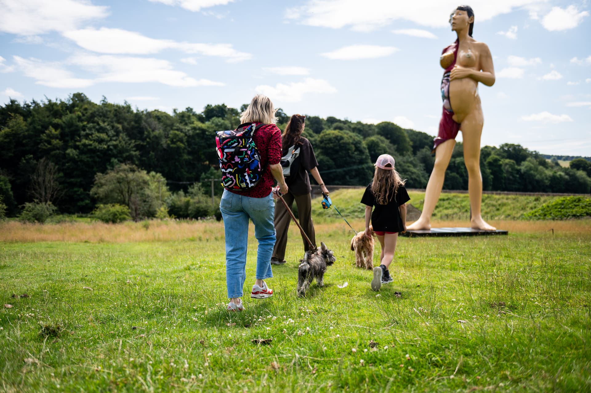 Family walking dogs near large modern sculpture in green field