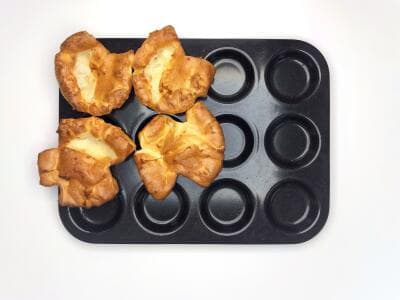 Four golden Yorkshire puddings in a black baking tray