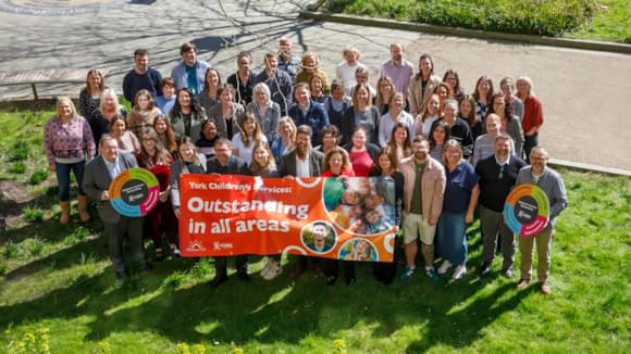 Group of people holding 'Outstanding in all areas' banner outdoors