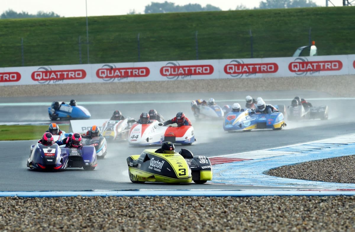 Motorbike sidecar race on wet track with spectators in background