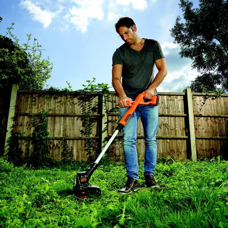 Man using an orange trimmer in a grassy backyard