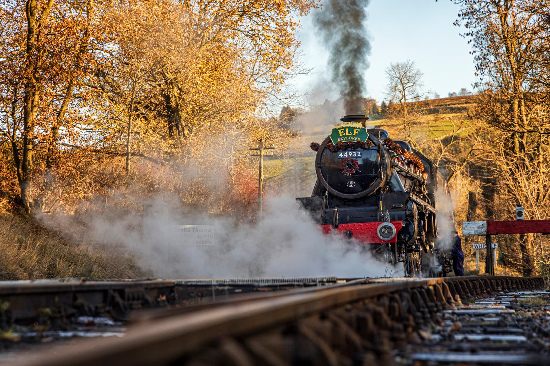 Steam train on rural track with autumn trees and hills
