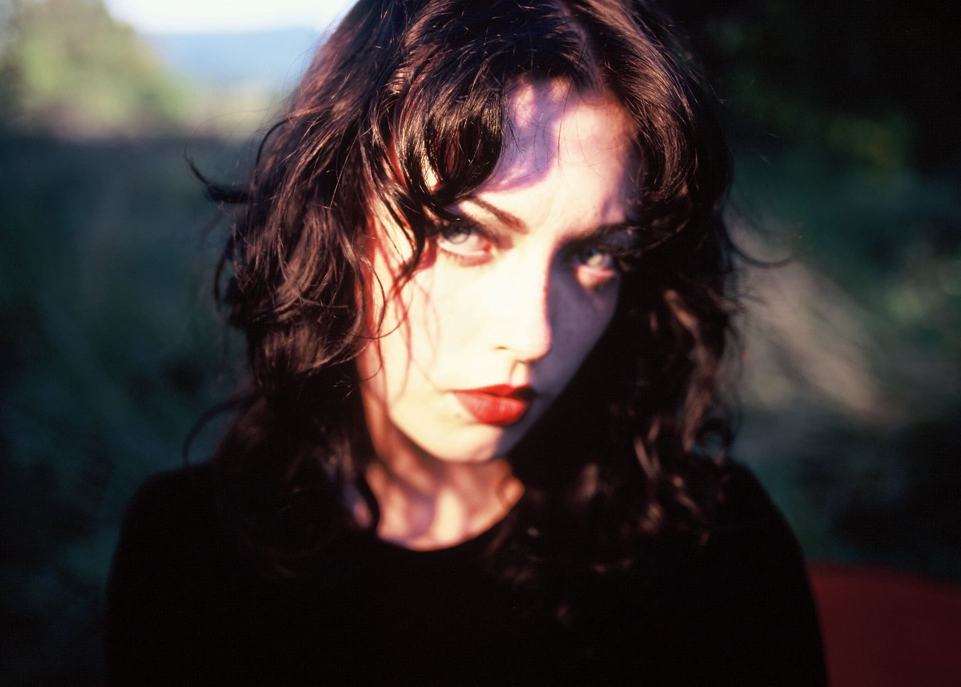 Woman with dark curly hair in shadowy outdoor setting
