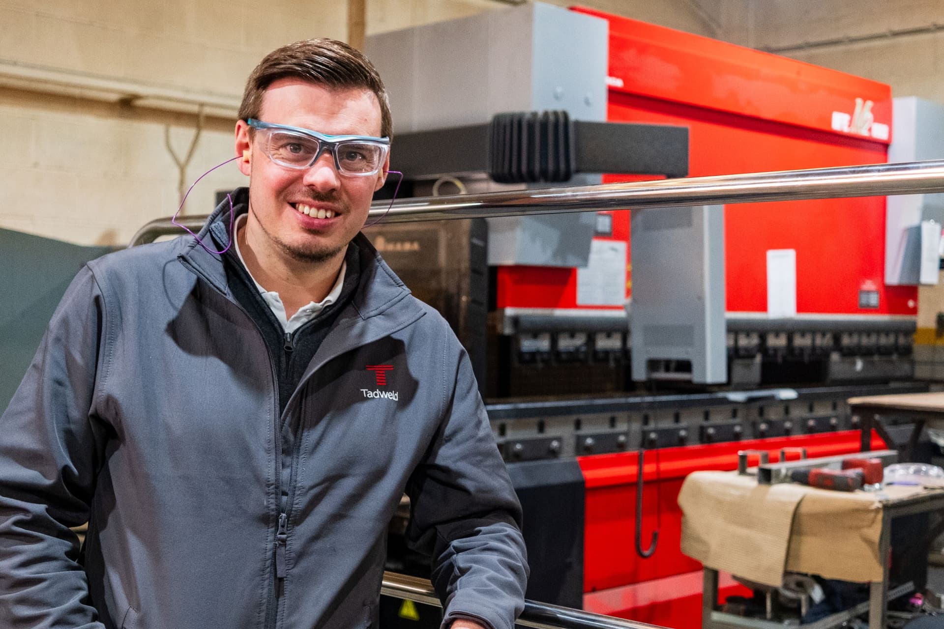 Man in grey jacket and safety glasses in metal workshop