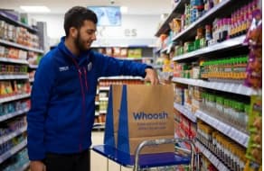 Store employee in uniform placing items in delivery bag
