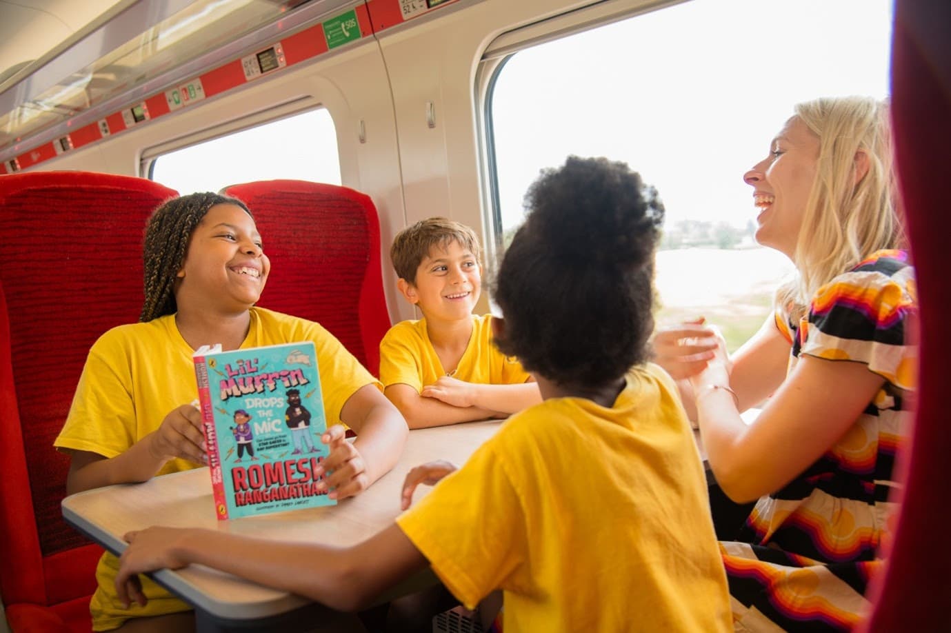 Family laughing and reading on a train with red seats