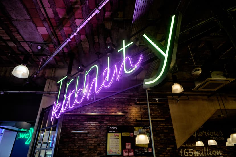 Neon sign reading 'Trinity Kitchen' on brick wall