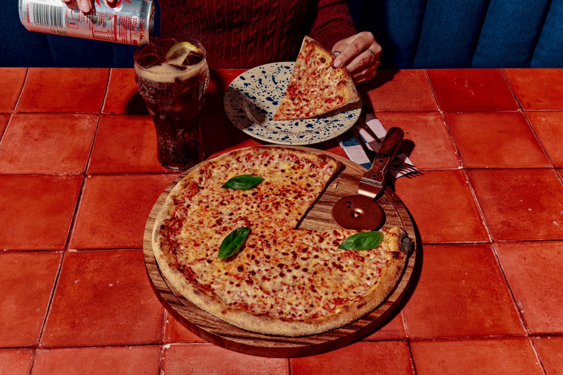 Person enjoying pizza with a drink on a terracotta table