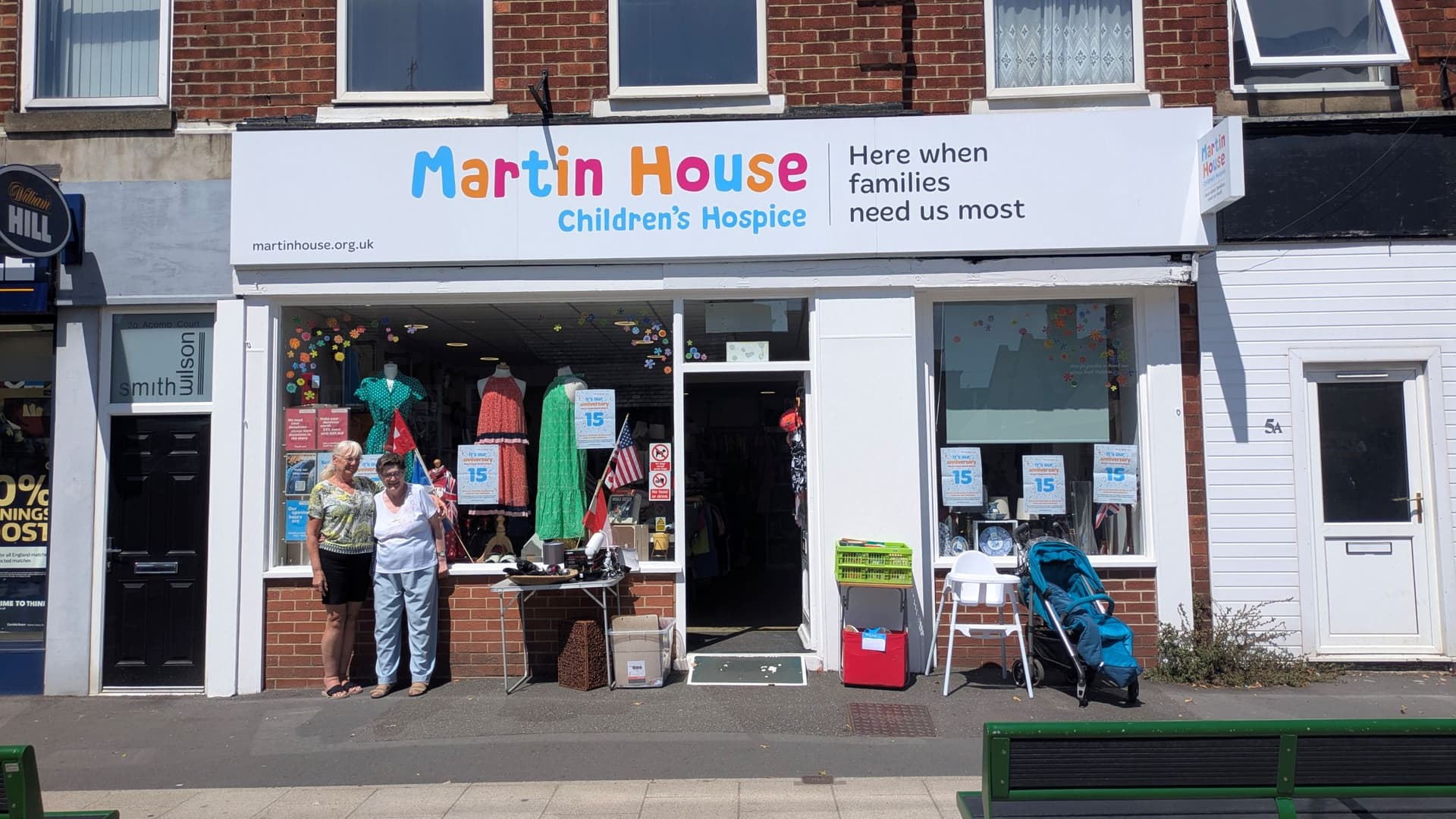 Martin House charity shop with colourful window display and two people outside