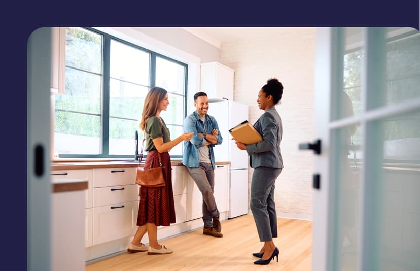 Three people engage in conversation in a bright, modern kitchen with large windows and warm wooden floors.