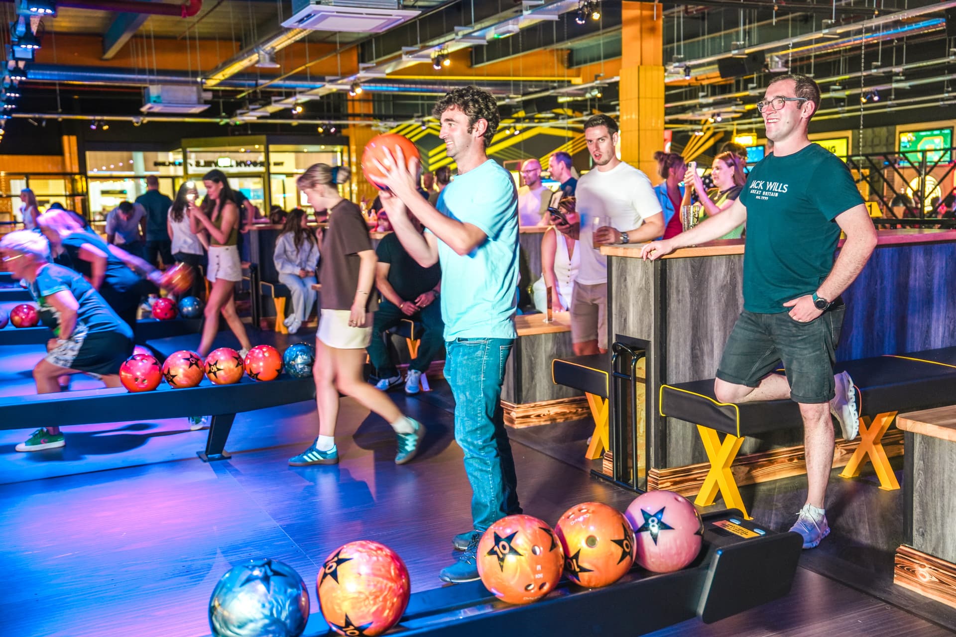 People bowling in a lively, colourful indoor alley with neon lights