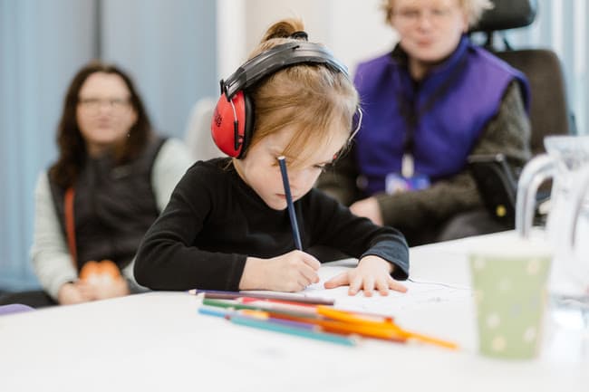 Young girl with red headphones drawing at a table