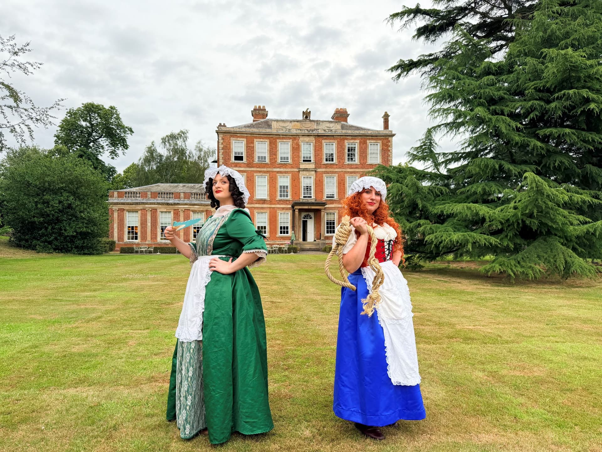 Two women in period costumes in front of a Georgian mansion
