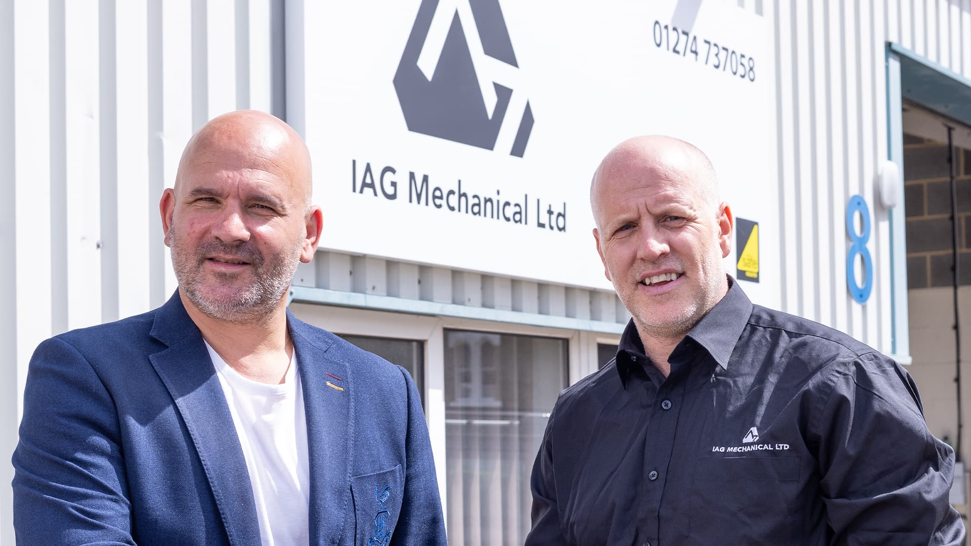 Two men in front of industrial building with company sign