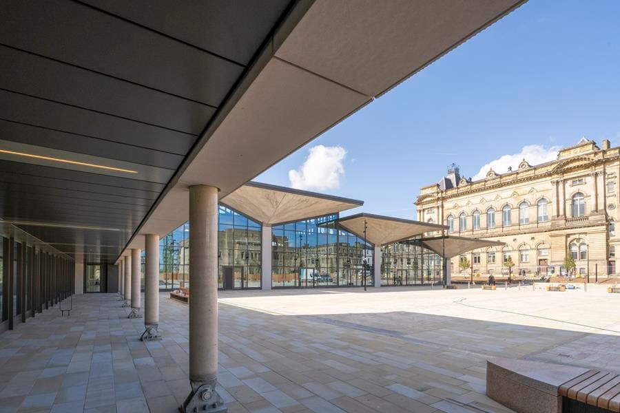 Modern glass pavilion with historic stone building in background