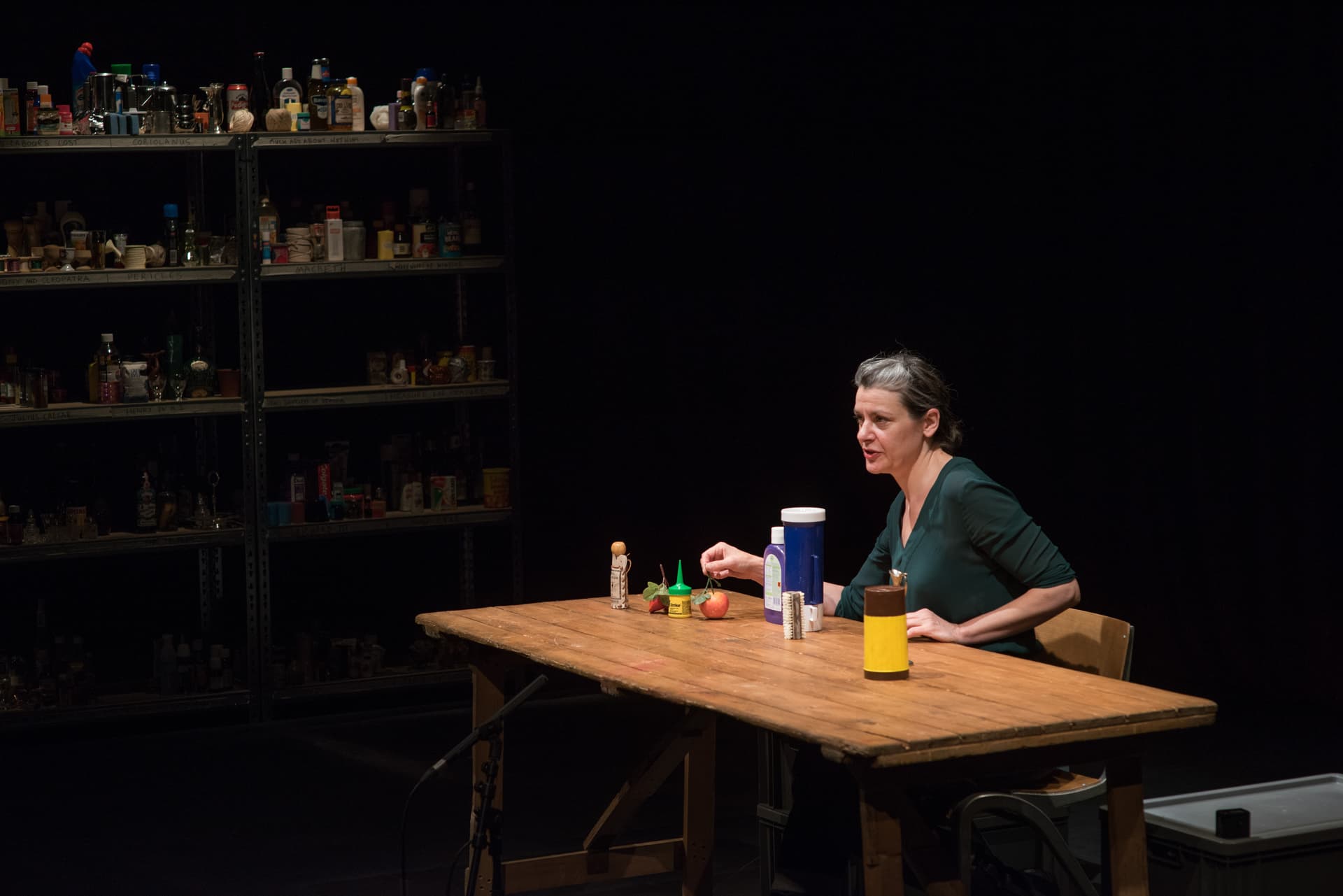 Woman performing at a wooden table with shelves of bottles